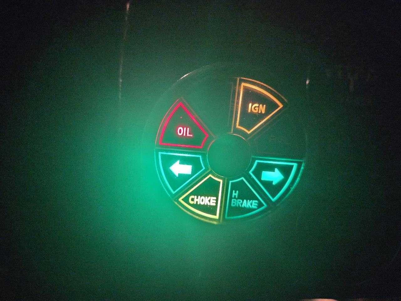 A Lucas warning-light cluster glowing green in the dark, with oil, ignition, indicator arrows, choke and handbrake segments lit.